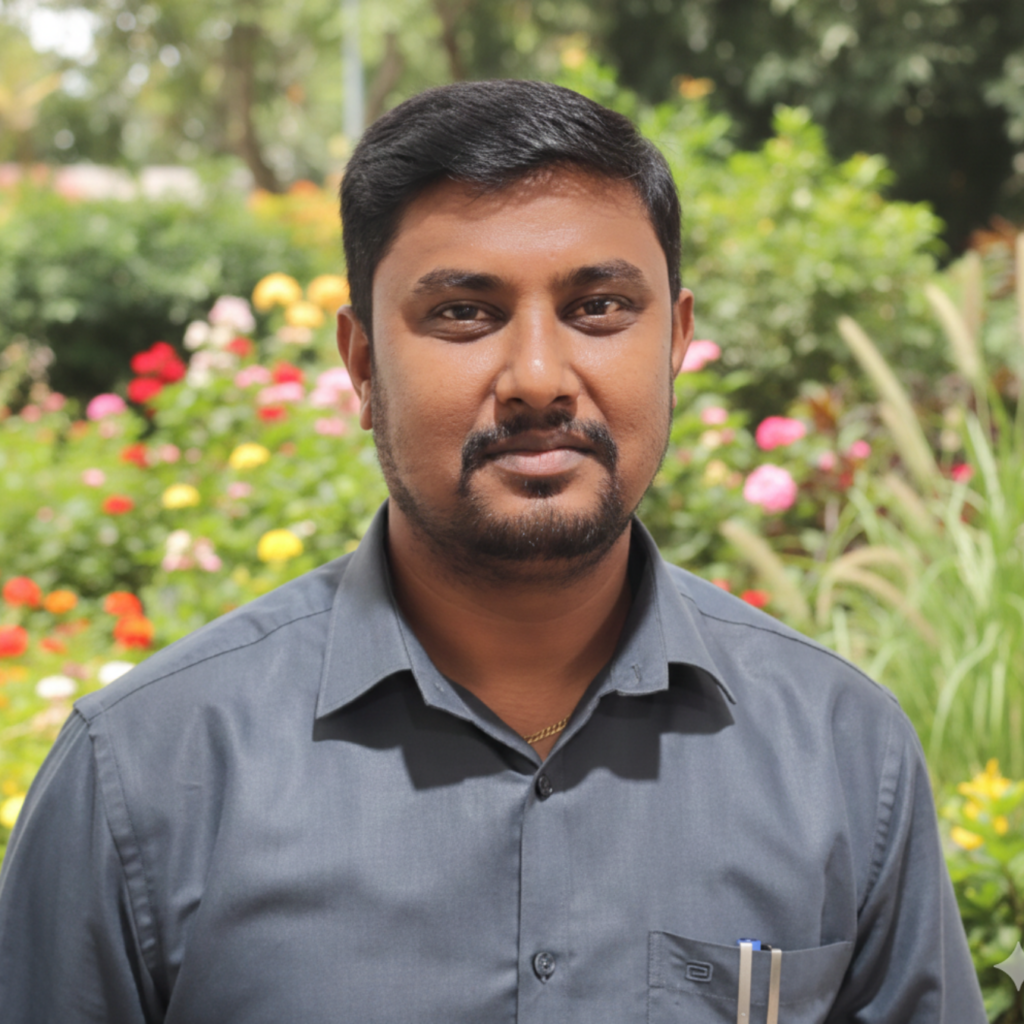 A man in a grey shirt with pens in his pocket standing in front of a flower garden.